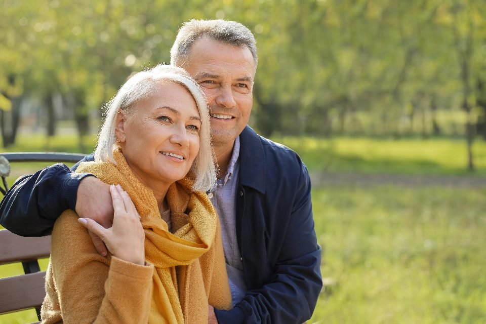 A smiling mature couple embraces on a park bench, illustrating date singles over 50 finding connection.