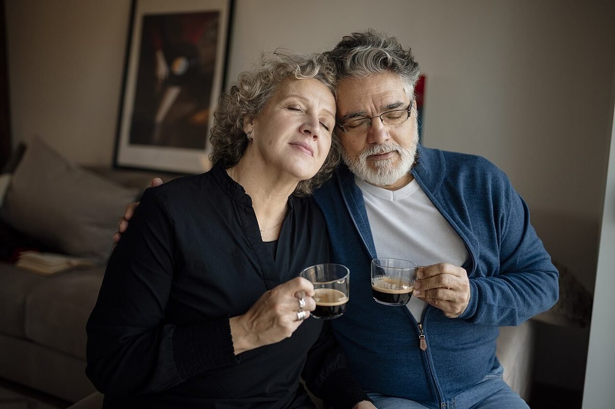 Older couple leaning close together and holding glasses of coffee, illustrating older jewish singles reviews.