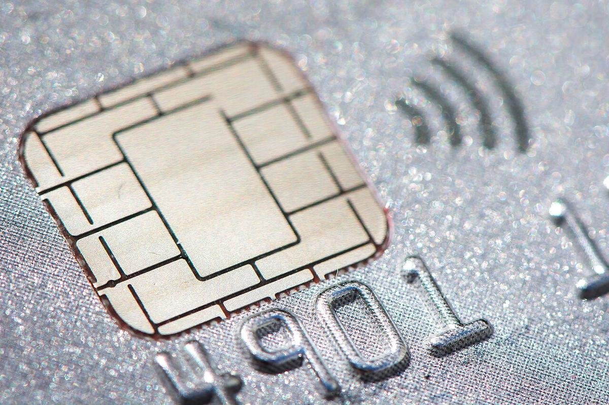 Close-up of a silver credit card showing a gold EMV chip, a contactless payment symbol, and embossed card numbers.